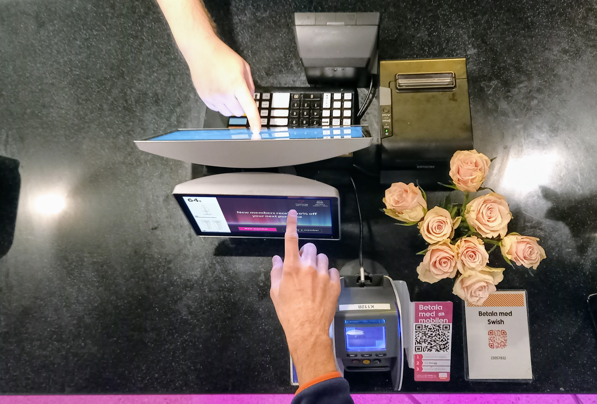 Customer and employee using two touchscreens at a retail counter beside a display of flowers